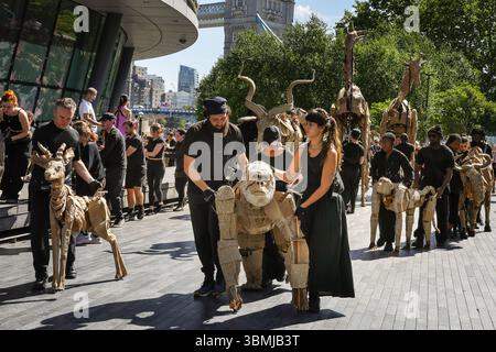 Londra, Regno Unito. 27 giugno 2025. Gli artisti camminano lungo il Bridge Theatre lungo il fiume Tamigi, oltre il vecchio Municipio e verso l'area degli spettacoli Scoop London. LE MANDRIE sono arte pubblica e azione per il clima. Da aprile ad agosto 2025, i burattini a grandezza naturale percorrono un percorso di 000 km dal bacino del Congo al Circolo Polare Artico, simboleggiando il loro volo dal disastro climatico con fermate in molte città e paesi, a Londra dal 27 al 29 luglio. Crediti: Imageplotter/Alamy Live News Foto Stock