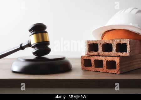 Concetto di giudizio relativo alla costruzione con martelletto e mattoni del giudice con casco protettivo su tavolo in legno e sfondo bianco isolato. Vista frontale Foto Stock