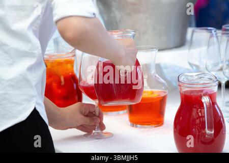 Servizio catering per preparare bevande per gli ospiti, versare succo di frutta rosso in un bicchiere durante un evento all'aperto Foto Stock
