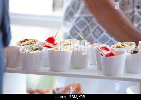 Piccole ciotole bianche piene di vari antipasti, tra cui riso, verdure e pomodori ciliegini, pronte per essere servite in occasione di un evento con servizio catering Foto Stock