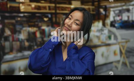 Giovane donna che indossa una camicia blu in un vivace mercato cittadino, circondata da vivaci negozi e bancarelle all'aperto, incarnano un senso di urban moderna Foto Stock