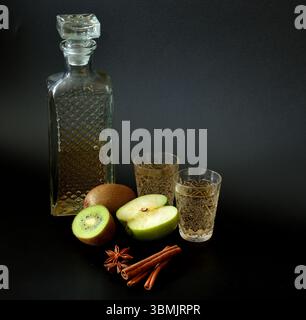 Liquore Kiwi con mela verde e spezie in cristallo su tavola nera, frutta, cannella e anice nelle vicinanze. Primo piano. Foto Stock