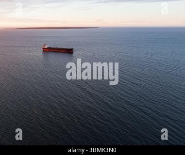 Un'epica veduta da droni di una nave da carico solitaria che naviga pacificamente nelle vaste e calme acque del Mar Baltico all'alba. Foto Stock