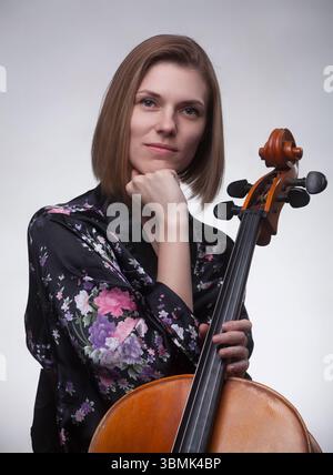 Donna caucasica, anni '20-'30, con un violoncello in un ritratto di studio. Indossa una veste floreale nera, appoggiando il mento sulla mano mentre guarda la cameriera Foto Stock