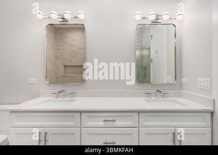 Bagno con armadio bianco, ripiano in marmo con rubinetti cromati e lampade moderne sopra gli specchi rettangolari. Foto Stock