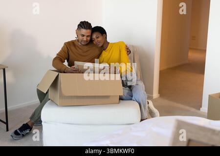 Con cornice per foto, diverse coppie sedute su ottomana in camera da letto, con scatola di cartone aperta Foto Stock