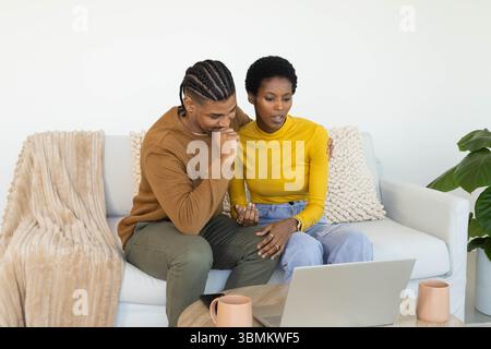 Coppia appoggiata seduta sul divano nel soggiorno, utilizzando un computer portatile su un tavolino da caffè in legno Foto Stock
