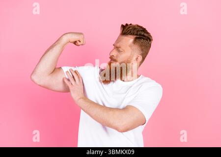 Uomo casual con barba rossa che si flette il braccio su sfondo rosa, per dare risalto allo stile di vita e alla moda Foto Stock