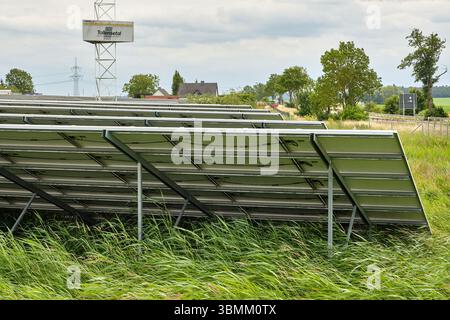 25 giugno 2024 - Altentreptow-Germania: File di pannelli solari su un campo verde vicino a un sito industriale sotto un cielo nuvoloso nel Meclemburgo, evidenziando re Foto Stock