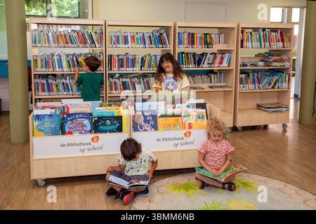 Paesi Bassi - bambini che cercano un libro e leggono libri nella biblioteca della loro scuola primaria. Foto Stock