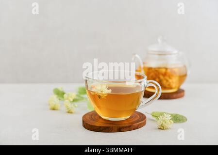 Tazza di tè al tiglio con teiera di vetro e fiori di tiglio su sfondo chiaro Foto Stock
