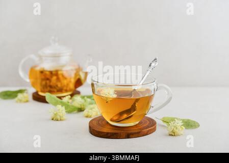 Tazza di tè al tiglio con teiera di vetro e fiori di tiglio su sfondo chiaro Foto Stock