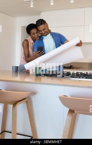 Esaminando coppie diverse nella moderna isola della cucina, rivedendo il progetto con lo smartphone Foto Stock