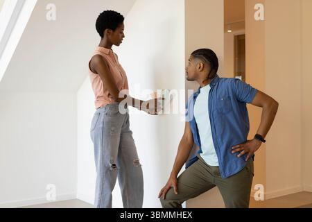 La scelta delle tonalità di vernice varia coppia si inginocchia accanto alla parete nel corridoio, tenendo il ponte dei campioni Foto Stock