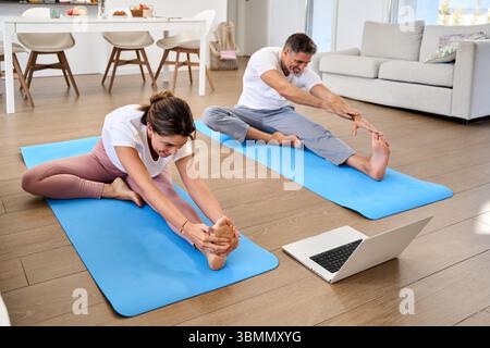 Indossate una coppia sportiva di mezza età che si allunga a casa guardando un notebook. Foto Stock