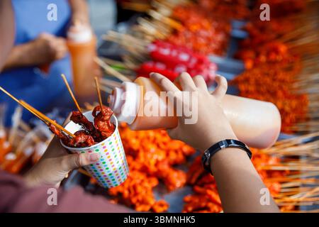 Spiedini di Street food filippini con salsa rossa in tazza di carta, salsa a mano al mercato all'aperto Foto Stock