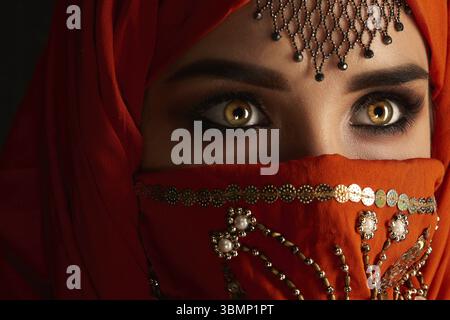 Ritratto ravvicinato di una giovane donna graziosa con bellissimi occhi fumosi e gioielli sulla fronte, che indossa l'hijab di terracotta decorato con paillettes Foto Stock