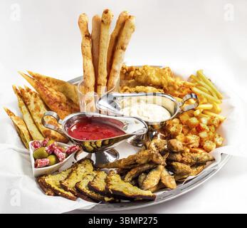 Piatto grande con un'ampia selezione di spuntini per la birra serviti con due tipi di salsa su sfondo bianco Foto Stock