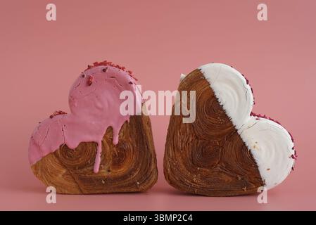 Due croissant a forma di cuore su sfondo rosa con spazio per le copie. Pasta sfoglia nuova pasticceria dolce alla moda. Esperimento di impasto cremoso Foto Stock