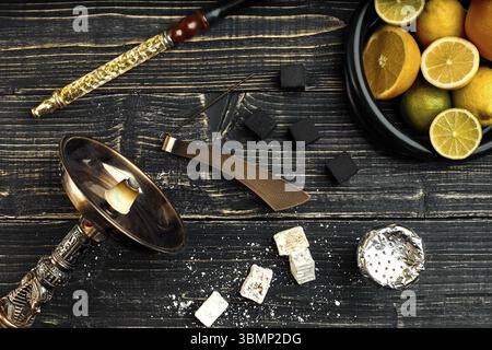 Elegante di fumare narghilè e il cestello con il limone, calce e arancione su sfondo di legno. Vista dall'alto. Lay piatto. Copia dello spazio. Still Life Foto Stock