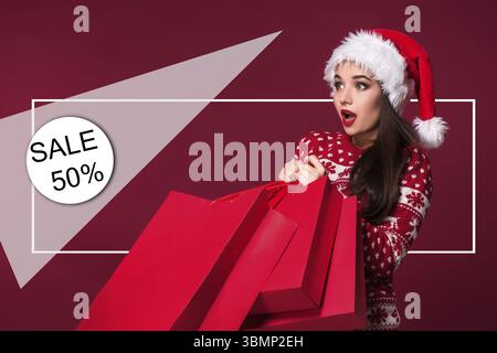 Donna di natale. Modello di bellezza ragazza in santa hat su sfondo rosso. Divertente ridere sorpreso ritratto di donna. A bocca aperta. Emozioni vere. Labbra rosse e essere Foto Stock