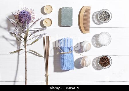 Set benessere con sale marino, olio essenziale, sapone e asciugamano decorato con fiori secchi su sfondo bianco di legno. Vista dall'alto. Spazio di copia. Vita morta. Simulazione. Foto Stock