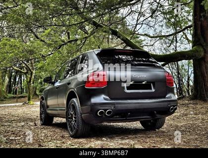 Vista posteriore di una Porsche Cayenne nera opaca parcheggiata in una foresta Foto Stock
