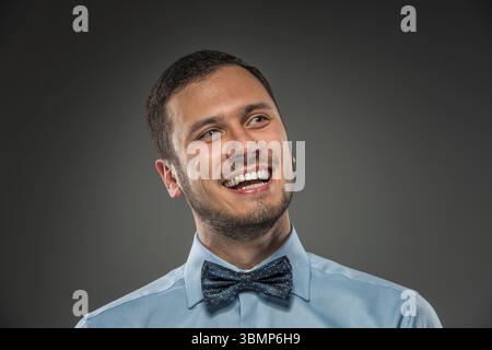 Ritratto di un giovane sorridente felice con camicia blu e cravatta a farfalla isolata su sfondo grigio studio. Primo piano Foto Stock