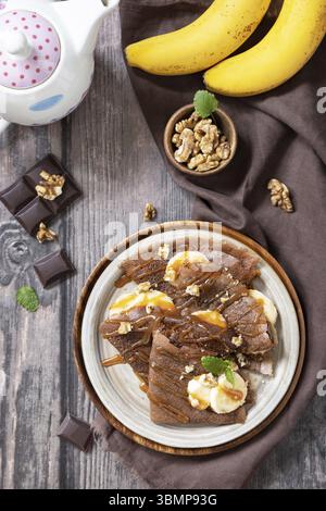 Festeggiamo la giornata dei pancake, colazione salutare. Deliziose crepe di cioccolato fatte in casa con noci, caramello, banane su un tavolo rustico in legno. Vista dall'alto, disposizione piatta Foto Stock