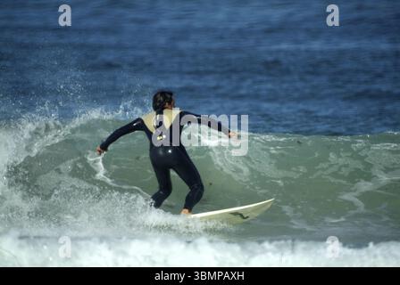 Surfista che cavalca un'onda nell'oceano indossando una muta Foto Stock