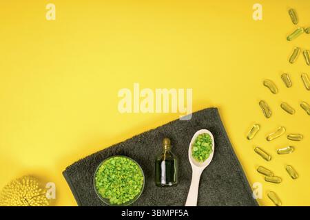 Set benessere: Sapone, maschera, olio, sale marino e asciugamano su sfondo giallo. Vista dall'alto. Vita morta. Spazio di copia Foto Stock