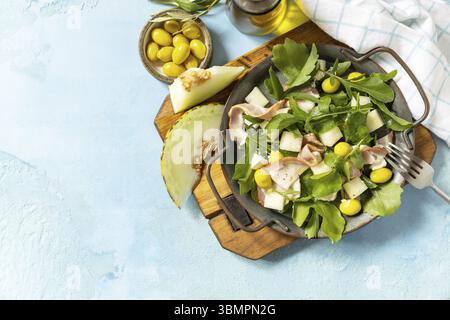 Antipasto tradizionale spagnolo e italiano. Insalata mediterranea estiva con melone, pancetta, olive, formaggio bianco e rucola su fondo di pietra blu. Vi Foto Stock