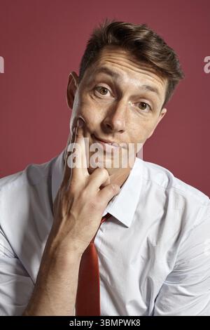 Ritratto ravvicinato di un interessante uomo brunetto con gli occhi marroni, indossato con una camicia bianca e una cravatta in terracotta. Sta guardando la telecamera mentre posi Foto Stock