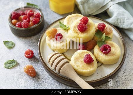 Frittelle di ricotta, tavolo colazione mattutino. Frittelle di formaggio cottage fatte in casa senza glutine (sciroppi, frittelle di cagliata) con frutti di bosco su fondo in pietra Foto Stock