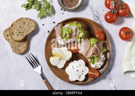 Colazione o brunch di Pasqua. Deliziosa prima colazione o spuntino - uova in camicia e formaggio panna toast pane integrale di segale di grano, prosciutto, rucola su una t di marmo Foto Stock