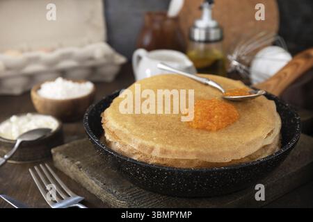Pancake cucina tradizionale russa. Sottili pancake in pizzo serviti con caviale rosso su un tavolo di legno Foto Stock