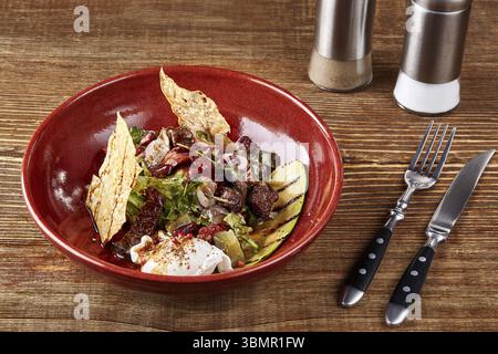 Insalata di diversi tipi di salsicce, cetrioli, peperoni, lattuga con salsa di panna acida in piatto su fondo di legno. Menu del ristorante. St Foto Stock