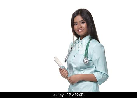 Ritratto di giovane donna medica indiana con stetoscopio intorno al collo isolato su sfondo bianco. Indossa l'uniforme acquamarina, guarda la telecamera Foto Stock