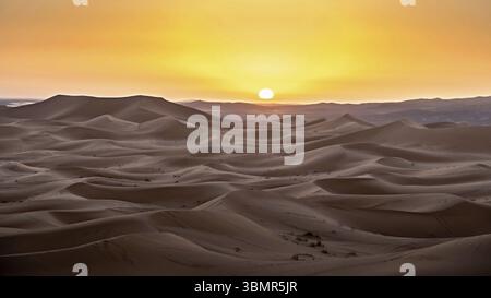 Vista panoramica del tramonto sulle vaste dune di sabbia ondulate nel deserto del Sahara, creando una calda luce dorata, un paesaggio tranquillo e accattivante Foto Stock