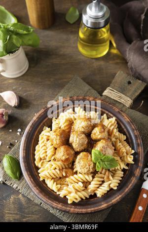 Cucina italiana fatta in casa. Fusilli italiani senza glutine con polpette di carne in salsa di pomodoro e basilico su tavola rustica. Copia spazio Foto Stock