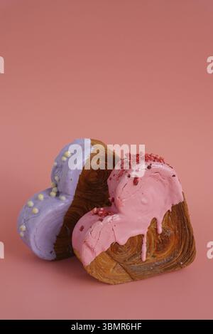 Due croissant a forma di cuore su sfondo rosa con spazio per le copie. Pasta sfoglia nuova pasticceria dolce alla moda. Esperimento di impasto cremoso Foto Stock