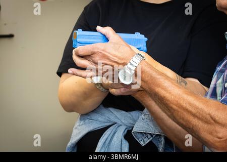 Landkreis Osnabrück, Deutschland 25. Juni 2025: IM Bild: In Instruktor oder erfahrener Sportschütze leitet eine andere person im sicheren Umgang mit einer Feuerwaffe an. für die Übung wird ein blauer Trainingsdummy in form einer Kurzhandwaffe verwendet. Die Hände beider Personen sind auf den Dummy gerichtet, wobei die Hände des Ausbilders die korrekte Griffhaltung demonstrieren oder korrigieren. DAS Bild unterstreicht die Bedeutung von praktischer Unterweisung und Sicherheitstraining im Sportschießen, insbesondere beim Erlernen des handlings von Feuerwaffen. Der blaue Dummy Dient als imperdibile Foto Stock