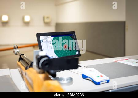 Landkreis Osnabrück, Deutschland 25. Giu 2025: Im Bild: Ein Schießstand wird aus der Perspektive des Schützen gezeigt, mit einem klassischen Holzschaft-Luftgewehr im Vordergrund, das auf einem Tisch aufliegt. Der Fokus liegt auf einem LCD-monitor im Mittelpunkt des Bildes, der eine digitale Zielscheibe und die Ergebnisse des Luftgewehr LG Auflage 30 Schießens anzeigt. Dies demonstriert Die Integration moderner elektronischer Zielerfassungssysteme in den traditionellen Schießsport. Rechts neben dem monitor befindet sich eine weiße Fernbedienung mit blauen und roten Akzenten, die zur Steuerung Foto Stock