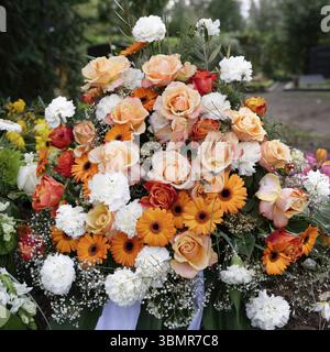 Eleganti fiori funebri di garofani bianchi, gerbera arancione e rose rosse e rosa su una tomba dopo un funerale Foto Stock