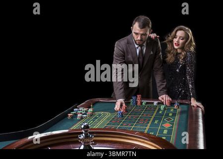 Un uomo con un vestito e una donna con un bel vestito nero che gioca alla roulette al casinò. Gioco d'azzardo. Casinò. Roulette. Poker Foto Stock