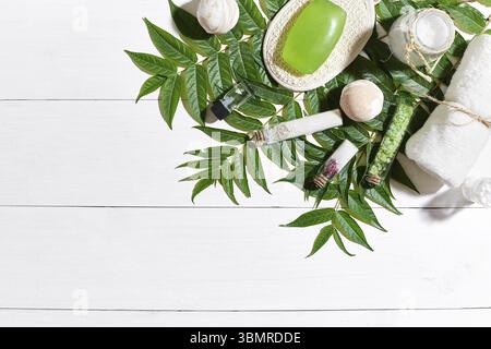 Set benessere con asciugamano e sapone su sfondo bianco di legno con foglie verdi. Vista dall'alto. Spazio di copia. Vita morta. Simulazione. Disposizione piatta Foto Stock