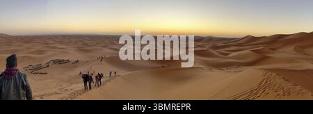 I turisti camminano sulle dune di sabbia nel deserto del Sahara al tramonto, godendo di una vista mozzafiato Foto Stock