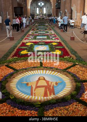 Alseno, Italia 22 giugno 2025 i visitatori religiosi ammirano il paesaggio ricoperto di fiori che circonda la statua di Cristo con le braccia sparse all'interno della storica Chiaravall Foto Stock