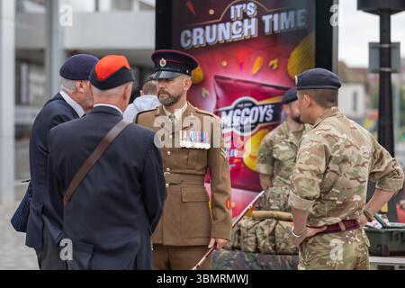 Southend on Sea, Regno Unito. 28 giugno, 2025.Un gruppo di militari britannici conversano in uno spazio pubblico urbano. Gli individui indossano un mix di uniformi mimetiche e formali, tra cui medaglie e insegne. Un annuncio di McCoy 's Crisps con lo slogan "IT'S CRUNCH TIME" è ben visibile sullo sfondo. Veterani, cadetti e organizzazioni in uniforme partecipano a una sfilata attraverso la High Street per onorare e celebrare la giornata delle forze armate. La parata termina a Victoria Circus per un servizio di ringraziamento. Penelope Barritt/Alamy Live News Foto Stock