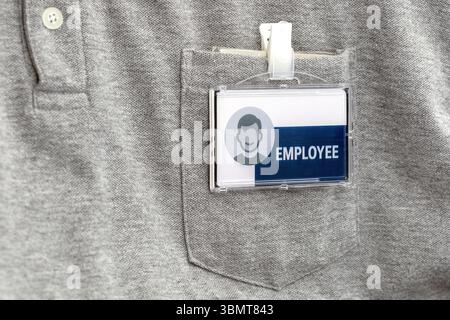 Una camicia grigia con il distintivo del dipendente agganciato alla tasca, con un'icona generica e la parola dipendente in primo piano. il badge è chiaro e professionale Foto Stock